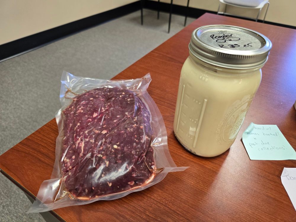 A desk with a slab of raw venison meat in plastic wrap and a mason jar of alcoholic eggnog on it. 