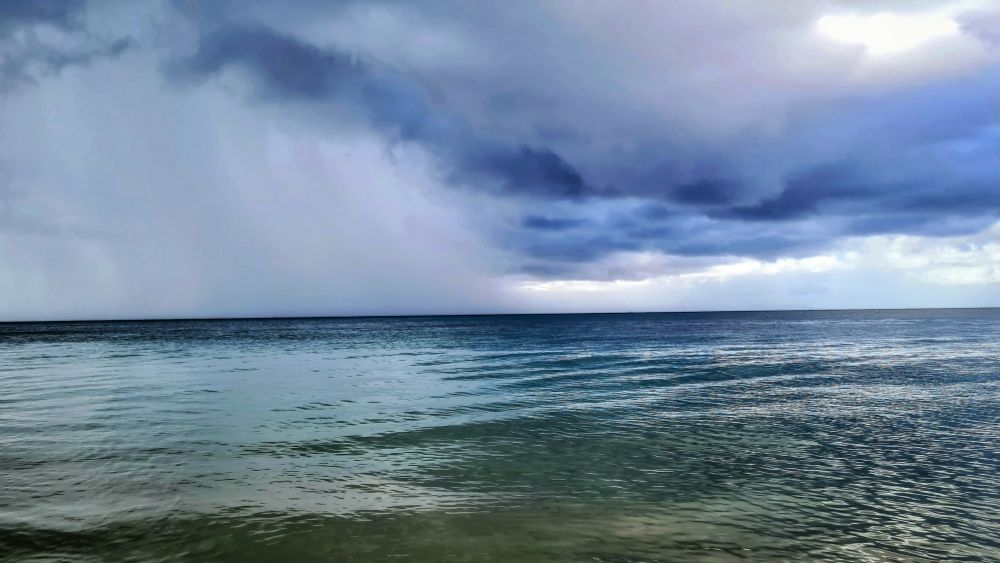 Guadeloupe.. Sur la plage,à l approche de l'orage.. Le ciel gris très menaçante reflète dans l'eau.  On aperçoit l averse qui balaye la mer au niveau de l horizon.