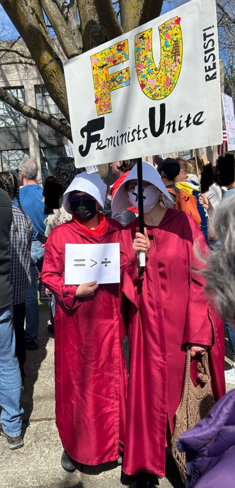 Protestors dressed in Handmaid’s Tale costumes holding a sign that reads “FU Feminists Unite”