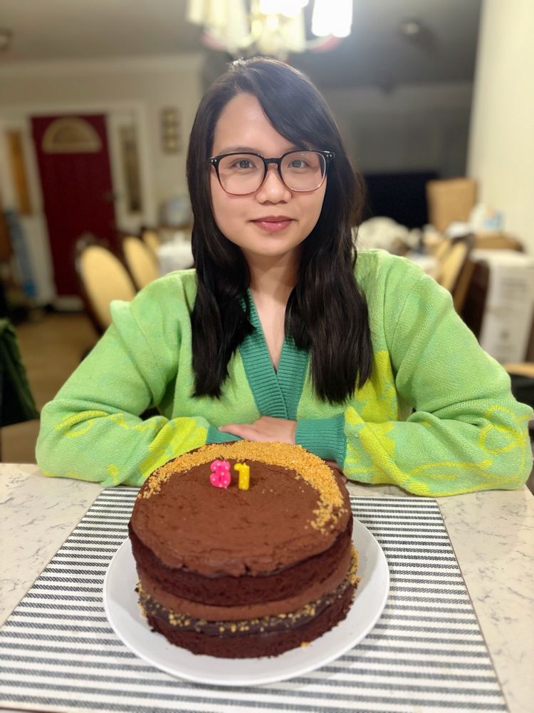 me in a green cardigan smiling in front of a two layer cake