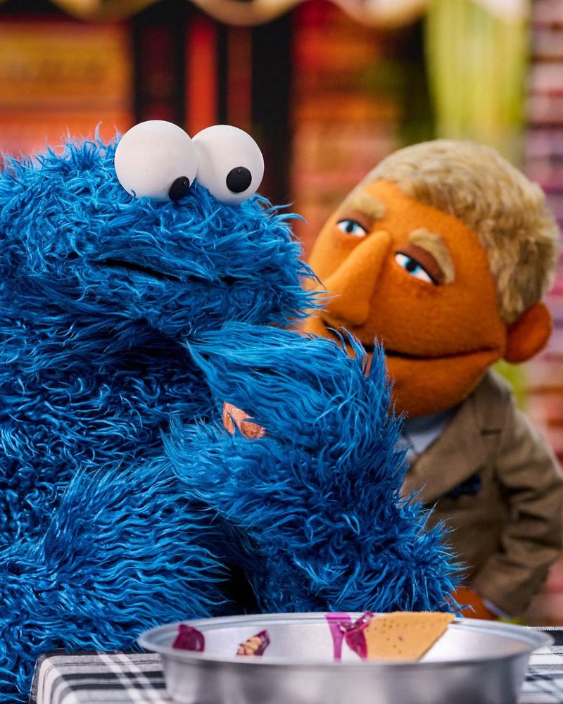 cookie monster looking at an empty pie pan with a muppet of daniel craig as benoit blanc in the background 