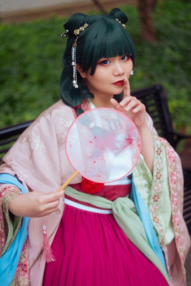a woman dressed as maomao in the apothecary diaries with a pink and green hanfu