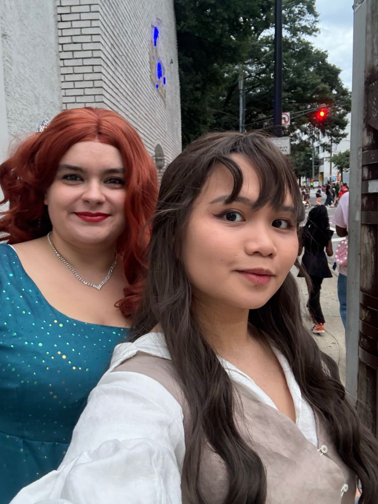 a woman in blue regency dress and curly red hair and a woman in wavy dark hair and a white shirt with a tan dress