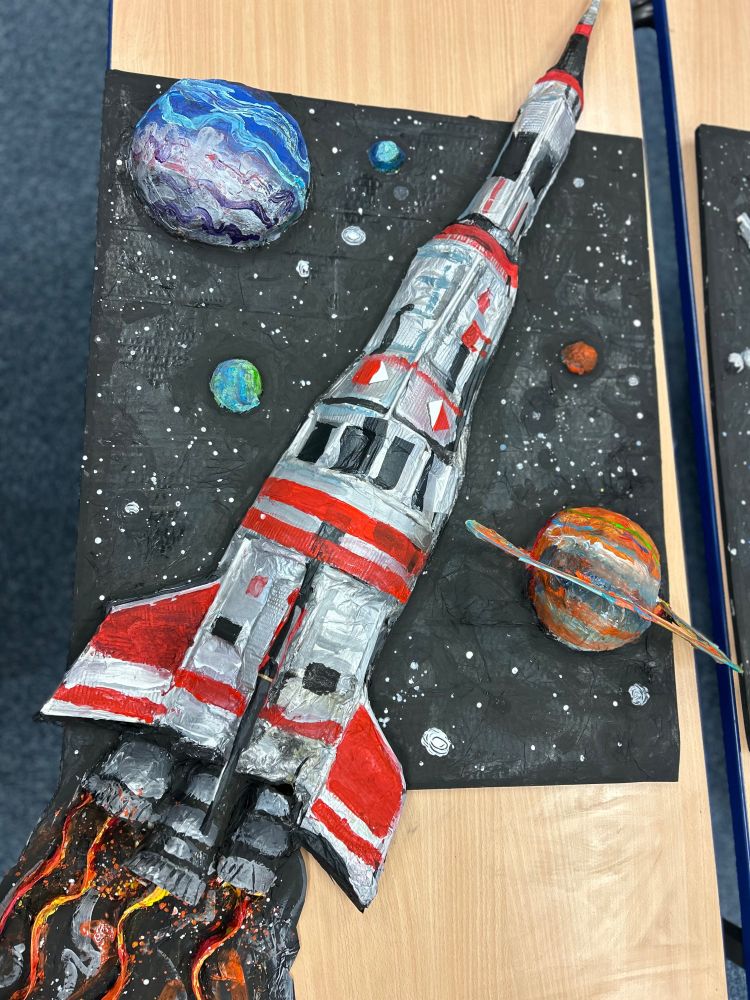 Space inspired artwork created by Year 5 pupils from Summerhill Primary School including an astronaut, a rocket, a 3D model of space probe 'Voyager 1', and a sculpture of the planets of our solar system. All of the work is made from cardboard and other scrap items, and then painted. Over 100 different children were involved in the building and decoration of all of the pieces. 