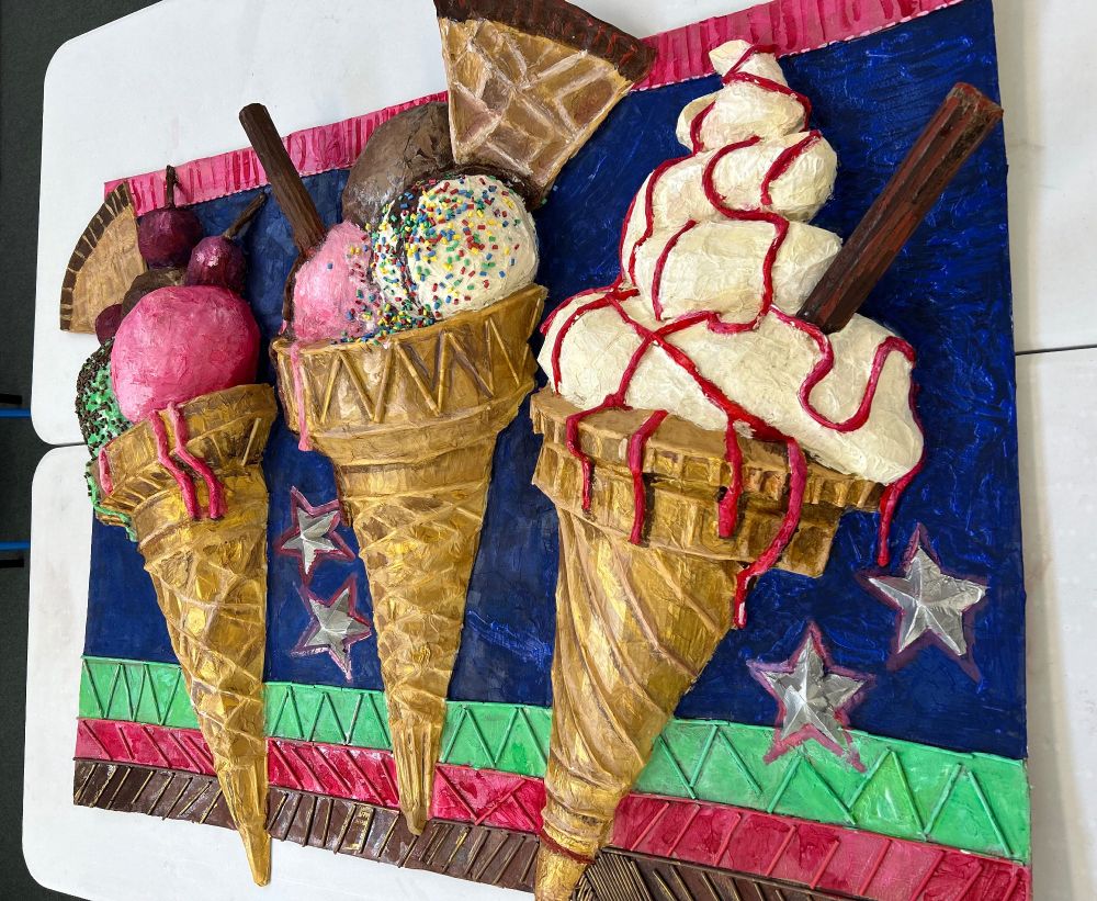A photo of the artwork created this week by the pupils at Marchant Holliday School in Somerset. The children built three large scale ice-creams, inspired by the painting s of Pop-Artist Wayne Thiebaud. The ice creams are made entirely from cardboard, paper straws, and tissue paper and have been painted with bright colours for the different flavours. The children also created a brightly coloured backdrop which makes them really stand out. 