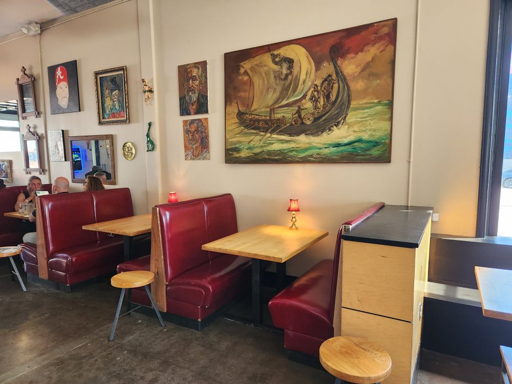 Two red leather restaurant booths with a large painting of a Viking ship on the wall above.