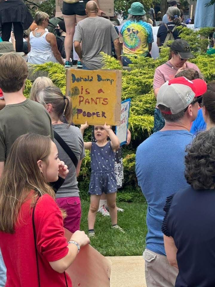 Young girl about 5 years old holds up a protest sign that reads “Donald Trump is a pants pooper”