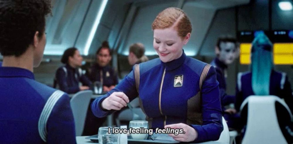 a woman in a blue uniform is sitting at a table with a man and says " i love feeling feelings " .