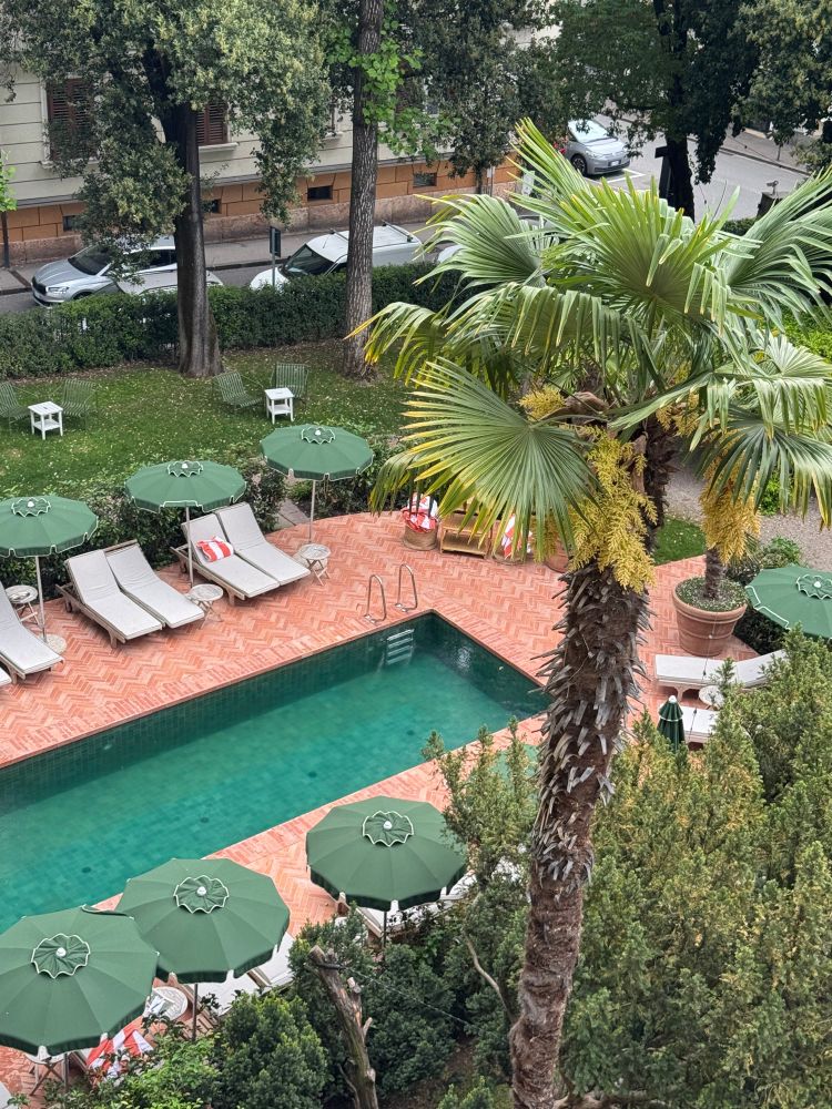 view from above showing an empty hotelpool sourrounded by deckchairs and a green garden