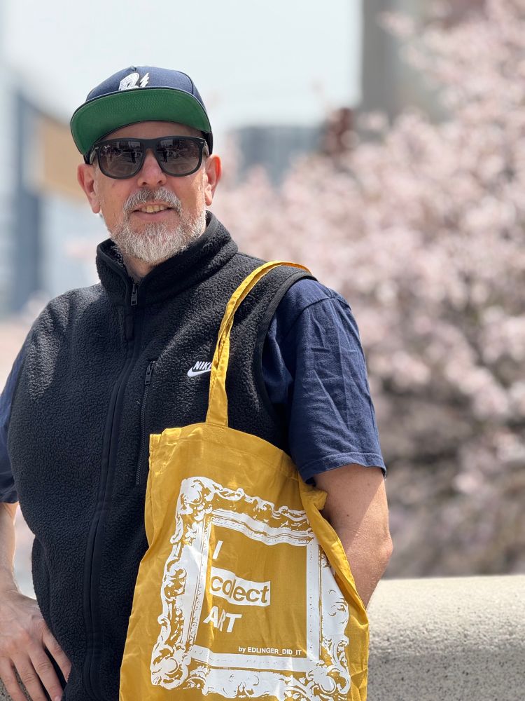 middleaged white guy posing in front of a cherry blossom tree in tokyo. A brown bag with a print that says ‚I collect art by edlinger_did_it‘ is hanging over his shoulder
