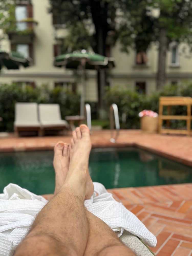 PoV of two male legs in front of an empty pool and a historical building in the back