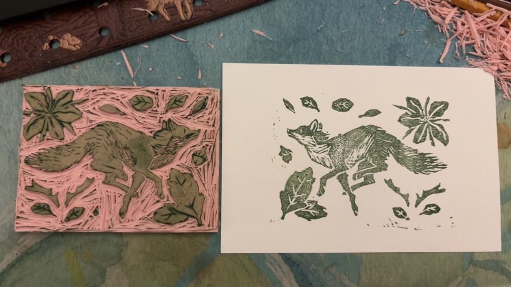 a blockprint and print of a fox surrounded by leaves, a blackberry flower, antlers, and an acorn