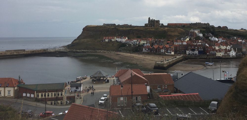 Photo of Whitby harbour, with the ruins of Whitby Abbey visible on top of the opposite hill