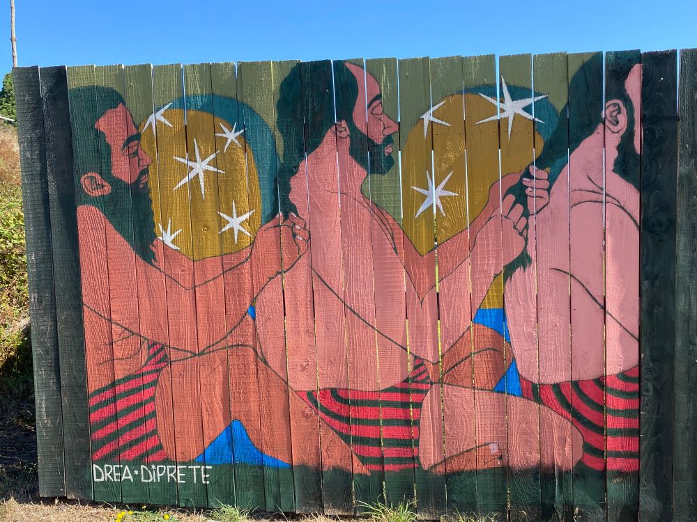 Three peaceful men braiding one another's hair. Downtown Port Townsend, old fence new murals. 