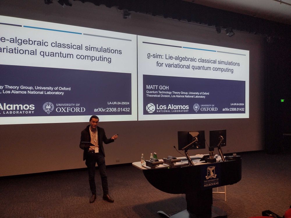 A photograph of me (Matt Goh) presenting a talk at the front of a lecture theatre. A title slide is present behind me, reading "g-sim: Lie-algebraic classical simulations for variational quantum computing".