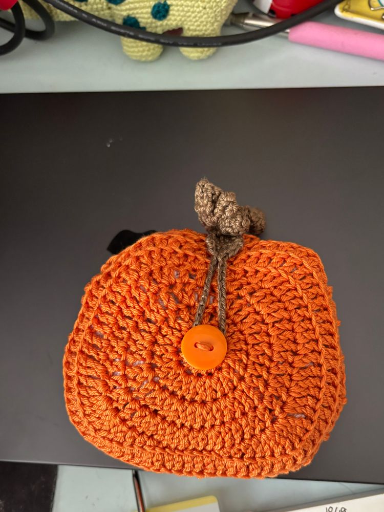 The bag folded into its orange pumpkin shape closed with a green leaf and loop that goes around a small orange button in the center of the pumpkin