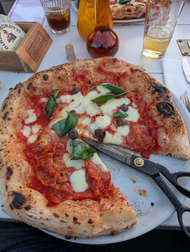 Pizza serviert mit einer Schere zu schneiden der Stücke, dazu Chiliöl und ein Bier