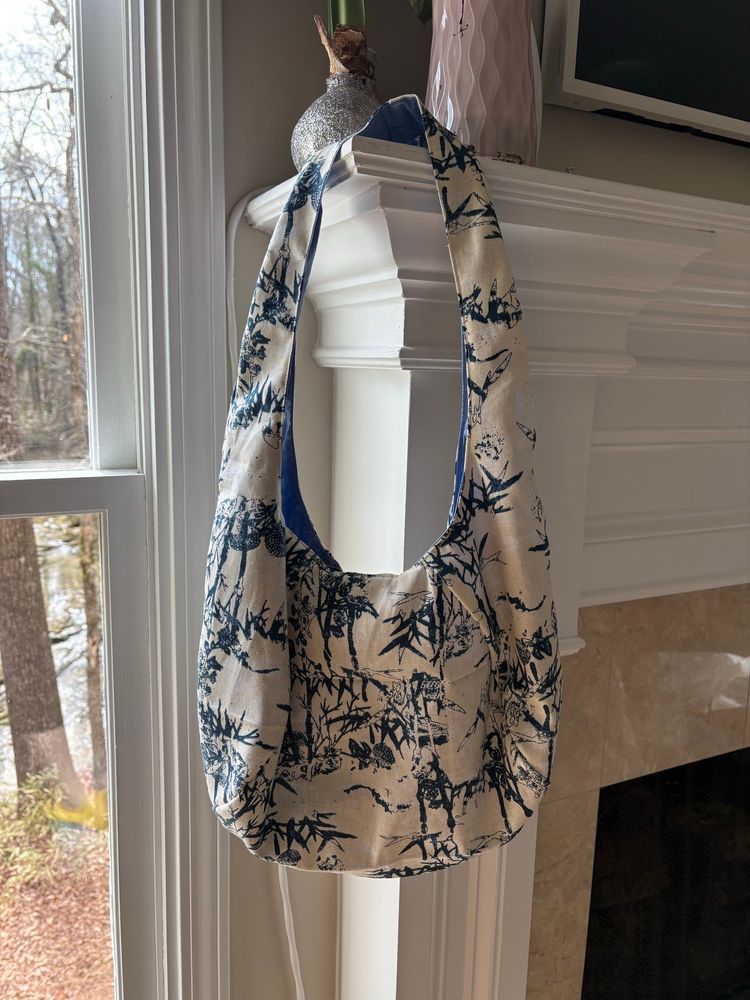 A blue & white shoulder bag hangs by the strap from the corner of a fireplace mantle. The bag has a relaxed, slouchy shape. 