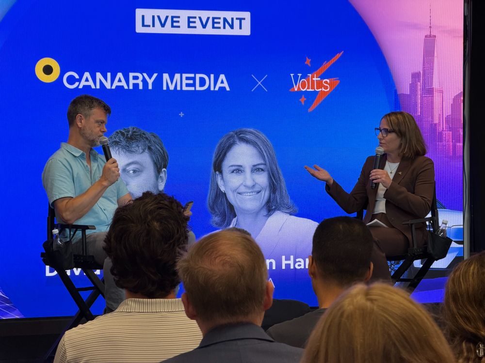David Roberts and Doreen Harris sit on a stage in directors' chairs in front of a bright blue background.