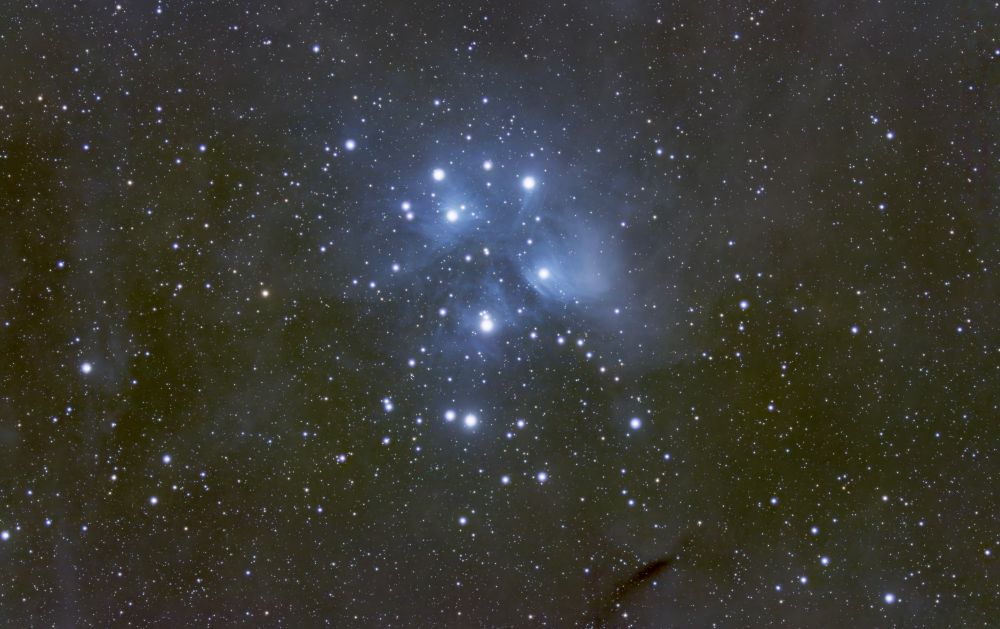 Blue nebulosity surrounding many stars forming an arrow like pattern pointing up in the image.