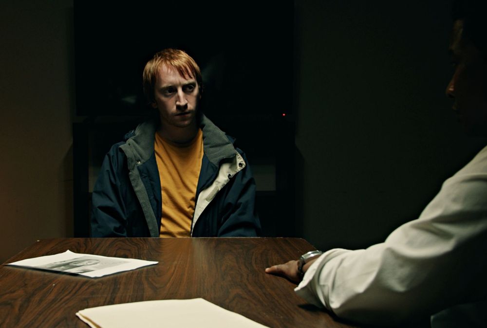 Cena do filme. Dois homens conversam numa mesa de escritório.