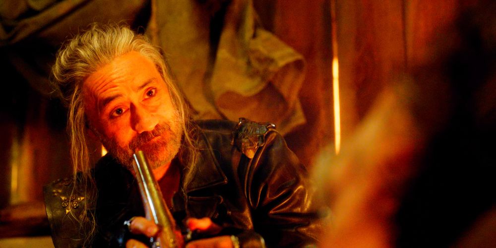 Ed Teach with his hair up, gentle and deranged, guiding Izzy in holding a gun to Ed's head. He's smiling at Izzy. They're in a hidden room in the Revenge.
