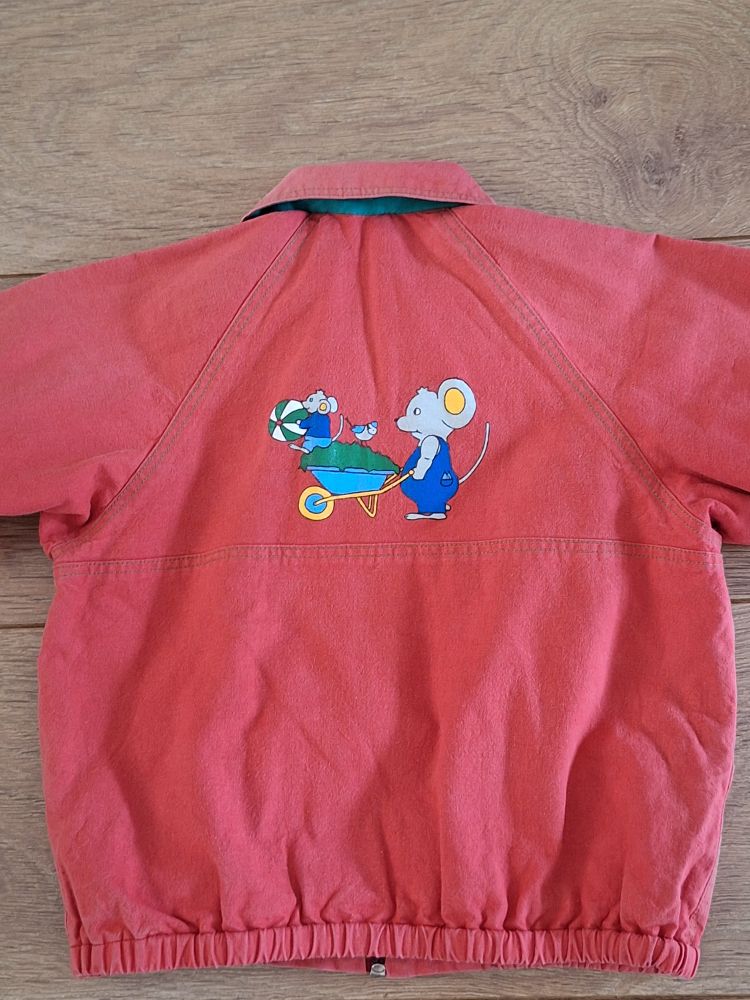 Children's jacket in red with a green lening and green buttons. On the back a picture, made with textile paint, of a daddy mouse pushing a wheelbarrow full of garden waste with a blue tit on top and a little mouse holding a ball. 