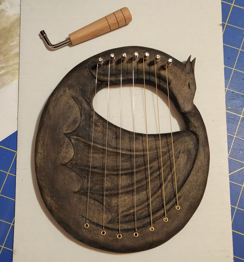 A small harp shaped like a dragon sleeping curled up with its tail tucked under its head and neck. It is stained a dark color and has 7 strings