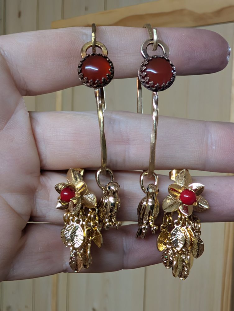 A pair of ear wrap type things with red stones set in them. A little brass bird charm hangs from each one. There is also a matching pair of earrings that have a flower with a red bead in the center, and a profusion of little brass leaves hanging from them