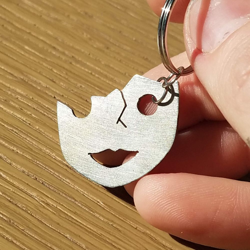 A nickel (silver tone) keychain in the shape of the bottom half of a broken mask