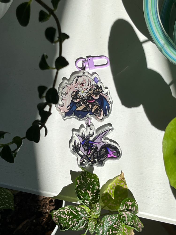 A photo of a linking charm showing female Corrin in her nohr noble outfit. She is linked to a charm of her nohr Dragon form. 
