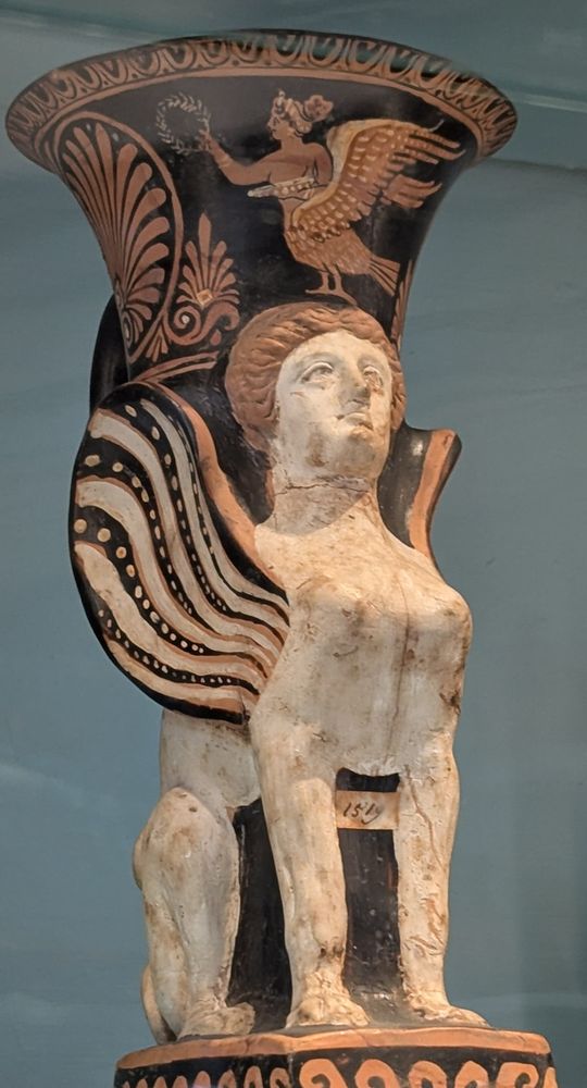 The rhyton is decorated with a sphinx with a white body, clay-colored hair, and black and white striped wings