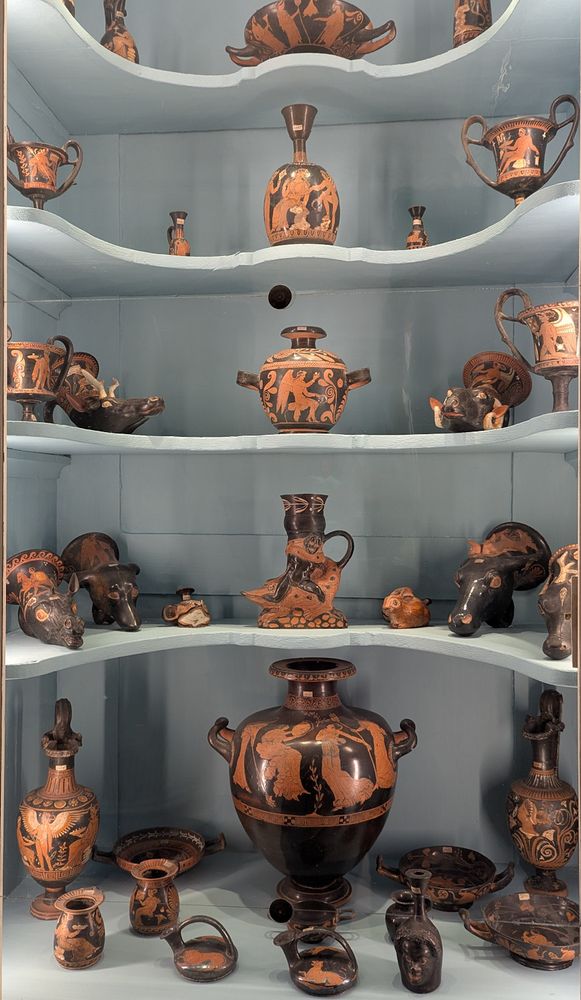 Cabinet behind glass with five shelves of red-figure pottery in different shapes