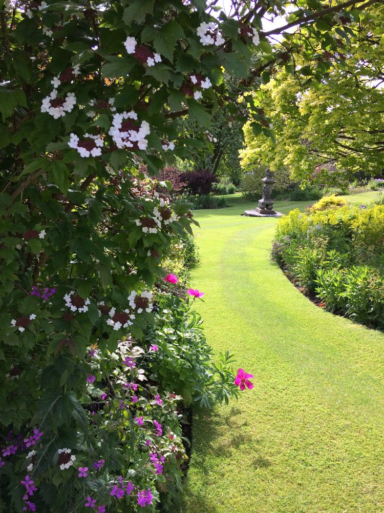 A curved section of an immaculate grass lawn with flowers and trees