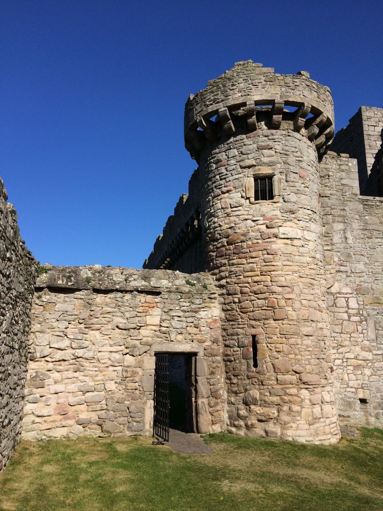 A view of a tower and wall with doorway of Craigmillar Castle. The tower has an arrow slit window on the ground floor and a small square window at the top