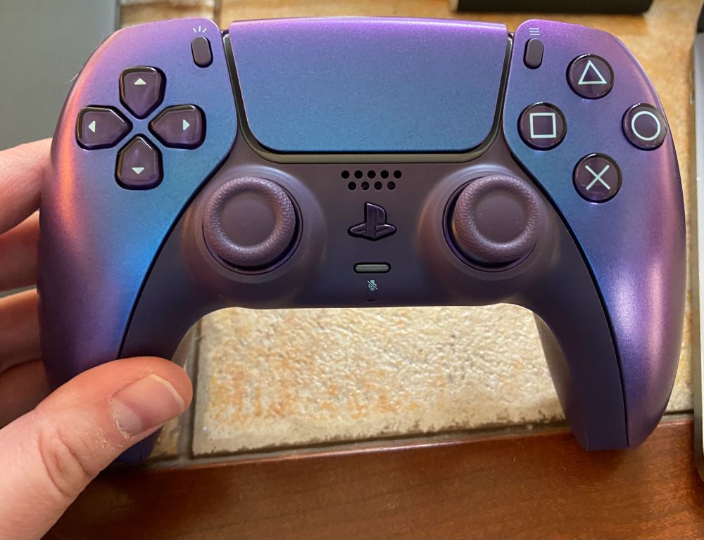 A hand holding a dualsense controller in a shiny blue-purple chrome color.