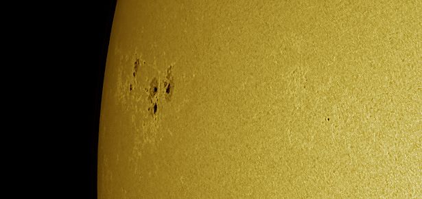 Telescope picture of a region of the Sun close to its limb where a few dark sunspots can be seen. Solar granules of a few thousand kilometers in size cover the Sun's surface, giving it the grainy texture we see in the picture.