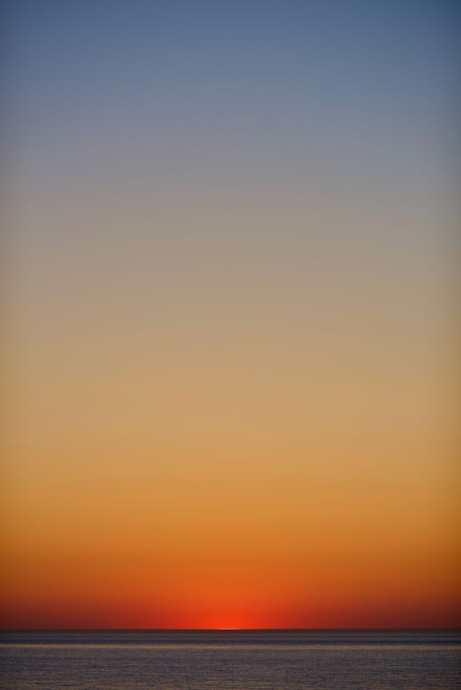 Photo of the North Sea, with a clear sky, right after the Sun went below the horizon. The sky has a degrade of colors from blue at the top to red at the horizon where it meets the sea.