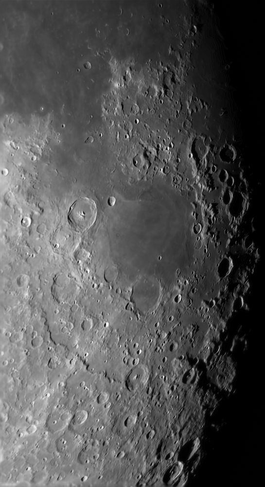 High magnification view of the moon's terminator during the waning gibbous phase using a telescope. It's a gray-scale image showing many craters and a relatively flat region near the center known as mare nectaris. 