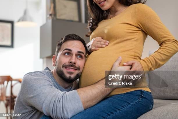Papa qui écoute le ventre de sa femme enceinte.