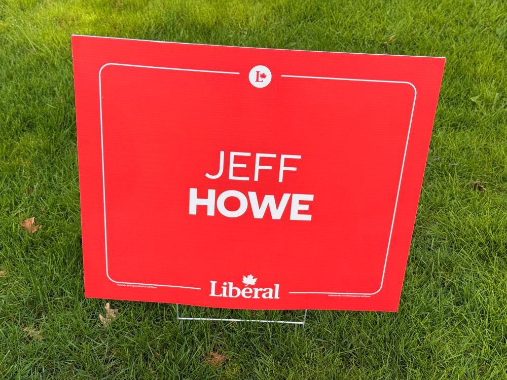 A red sign on a green lawn that reads: JEFF HOWE - Liberal”
