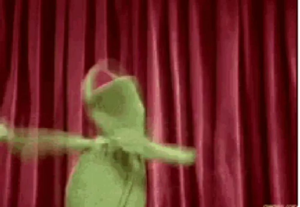 kermit the frog is dancing on a stage with a red curtain behind him .