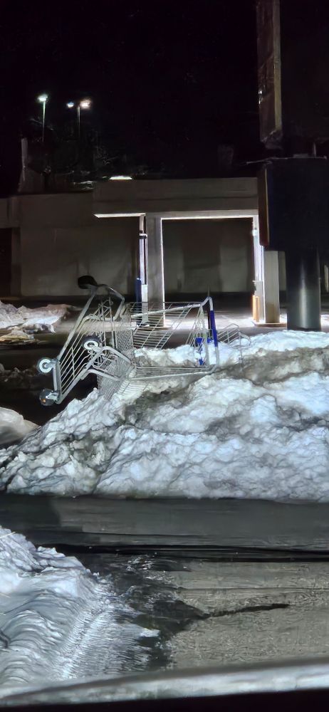 Photo of an overturned shopping cart half buried in the snow by the plows that cleared the parking area.