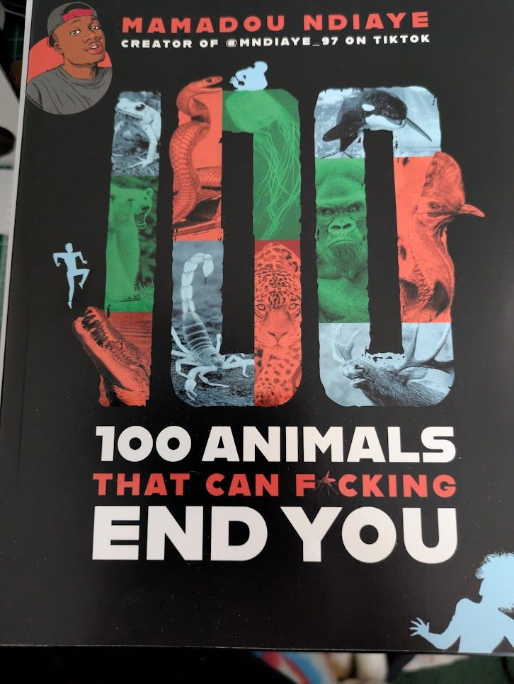 A book titled 100 Animals That Can F*cking End You. In larger text, the number 100 is filled with red, green, and grey images of animals. Across the top is a small circular cartoon image of author Mamadou Ndiaya, also known as Casual Geographic on Youtube, alongside his name.