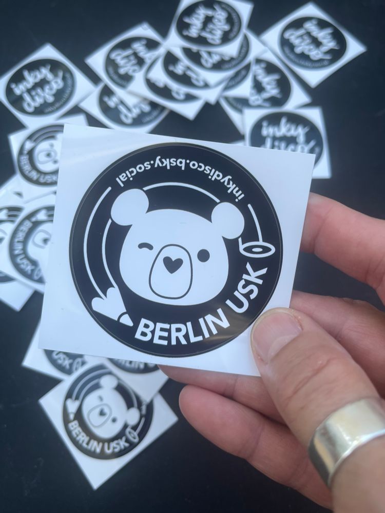 There’s a hand holding a sticker. In the background are smaller stickers laying on the ground.