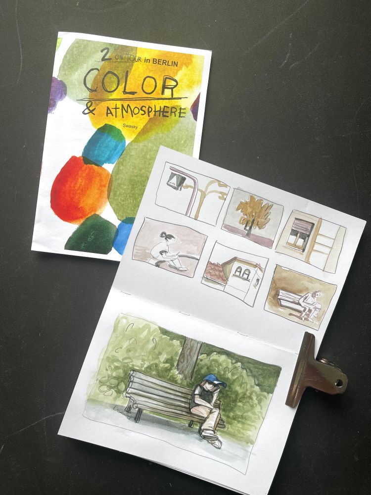 There’s a sketchbook with 6 thumbnail sketches on top. On the bottom page is a sketch of a person sitting on a bench, holding a mobile, wearing a 🧢. On the left is a handout zine of Swasky’s workshop about colours and atmosphere.