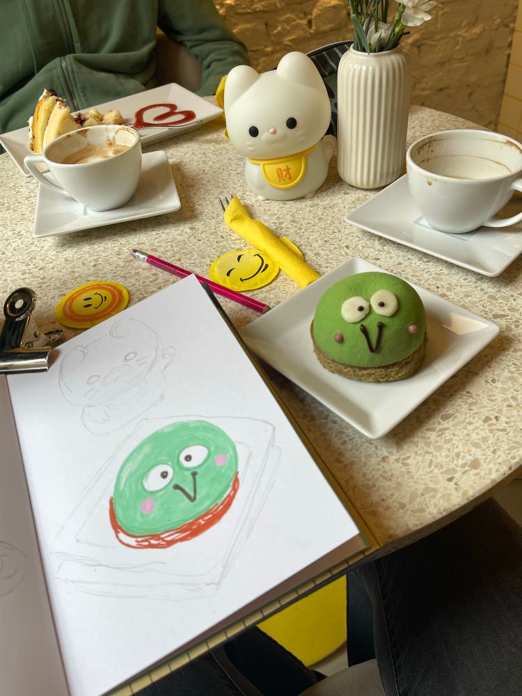 Our table with a sketchbook, green keroppi cake, empty coffee cups.