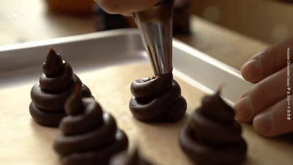 a person is piping chocolate into a tray of cookies that look like poop