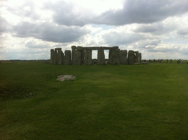 A picture of Stonehenge from a distance (well, the closest you can really get to it anymore unless you're an archaeologist). 

The field is very green with an overcast, grey sky. 