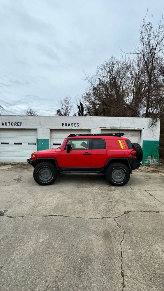Red 2012 Toyota FJ Cruiser Trail Teams parked in front of a derelict mechanic garage.